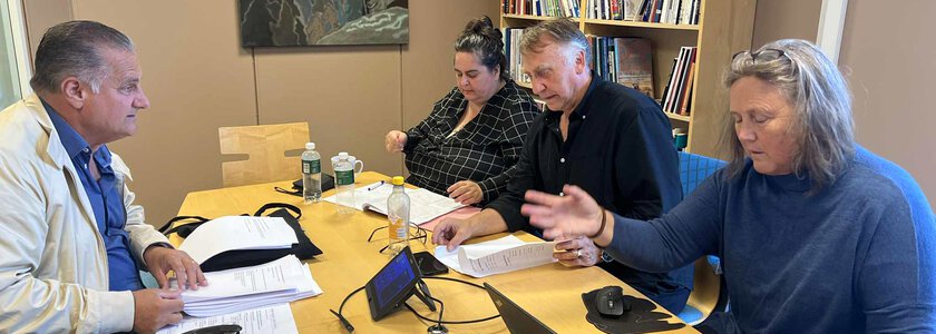 To kvinner og to menn sitter i samtale rundt et bord med dokumenter og papirer som de ser i  - Klikk for stort bilde