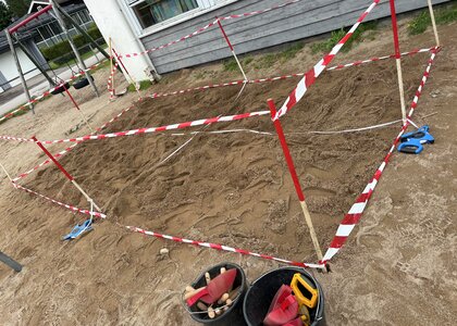 Rødt og hvitt bånd gjerder inn en sandkasse. - Klikk for stort bilde