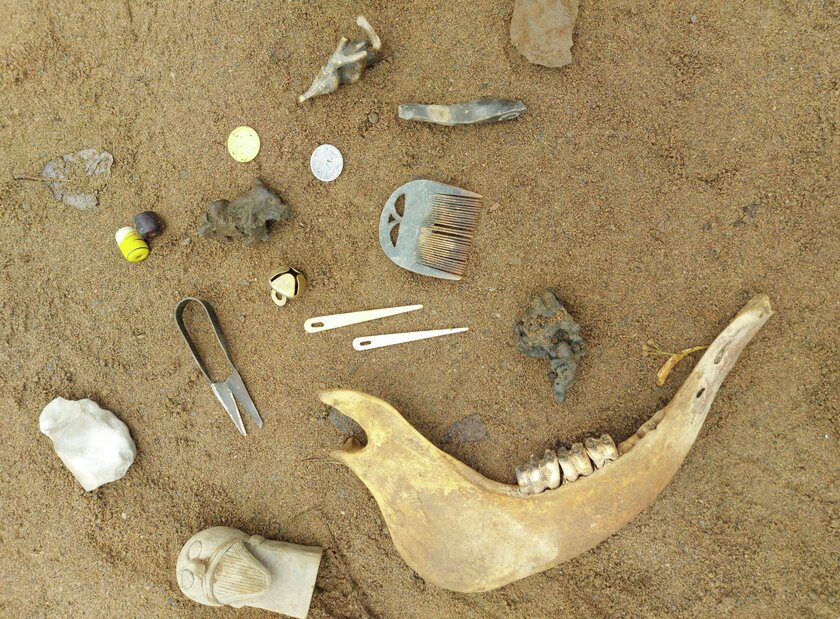 Gamle mynter, rester av en dyrekjeve, små skulpturer, hårkammer ligger utover sand. - Klikk for stort bilde